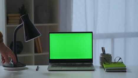 man-is-closing-cover-of-laptop-with-green-screen-on-table-freelance-and-home-office-working-place-of-writer-or-freelancer-in-apartment-detail-view-on-desk